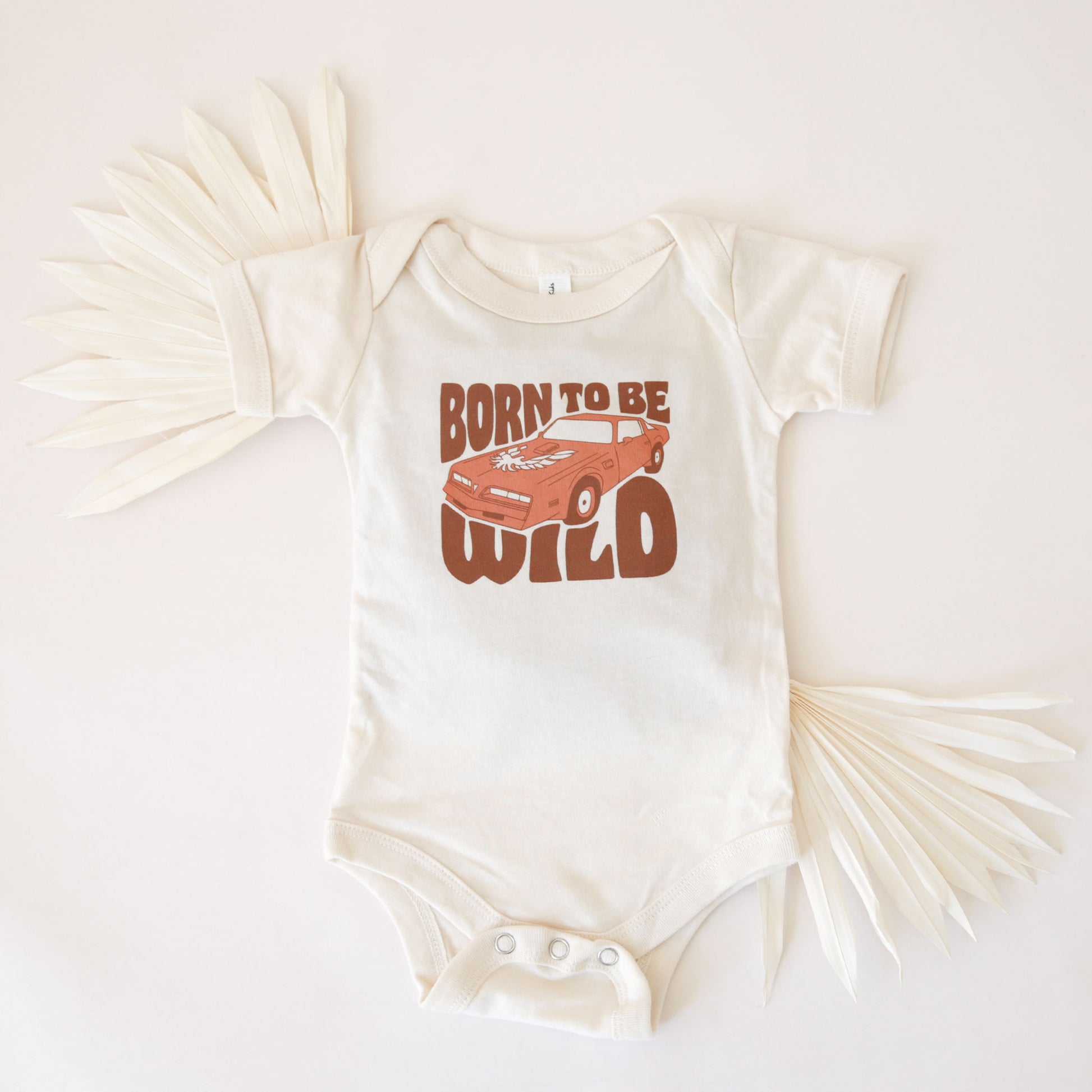 A white cotton onesie with a sports car and the text, "Born To Be Wild" in a brown groovy font.