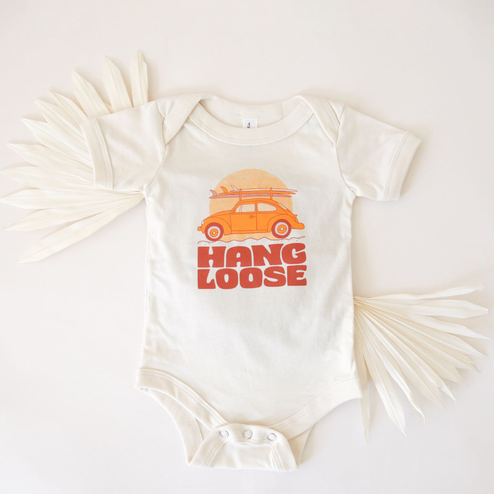 A white cotton onesie with the sweetest VW bug with surfboards and the text, "Hang Loose" burnt orange font.